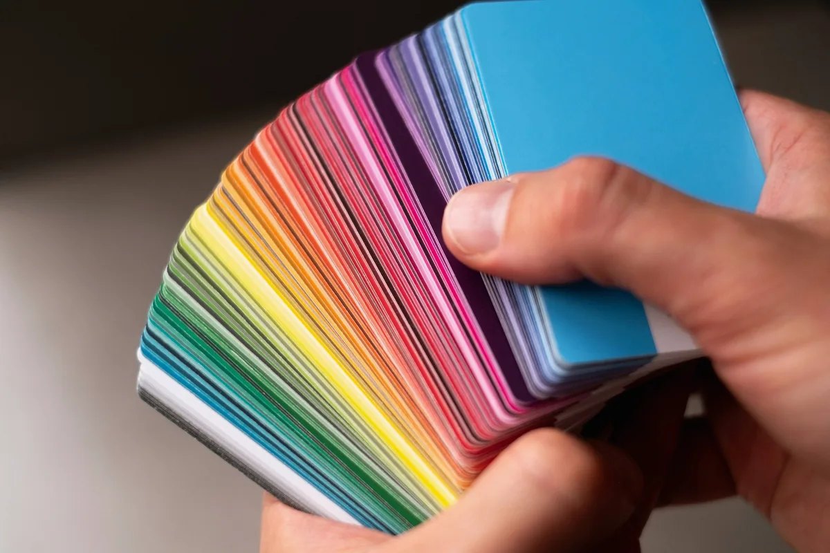Une main tient un éventail de nuanciers aux couleurs de l'arc-en-ciel